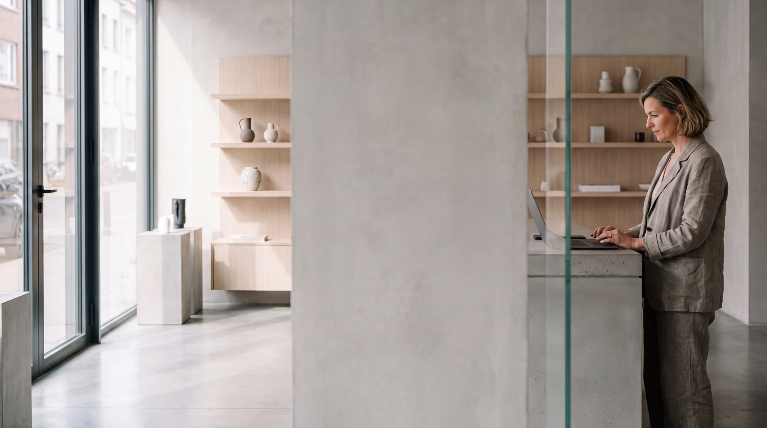 Une gérante de boutique travaille sur son ordinateur portable, debout au comptoir d'un magasin contemporain baigné de lumière