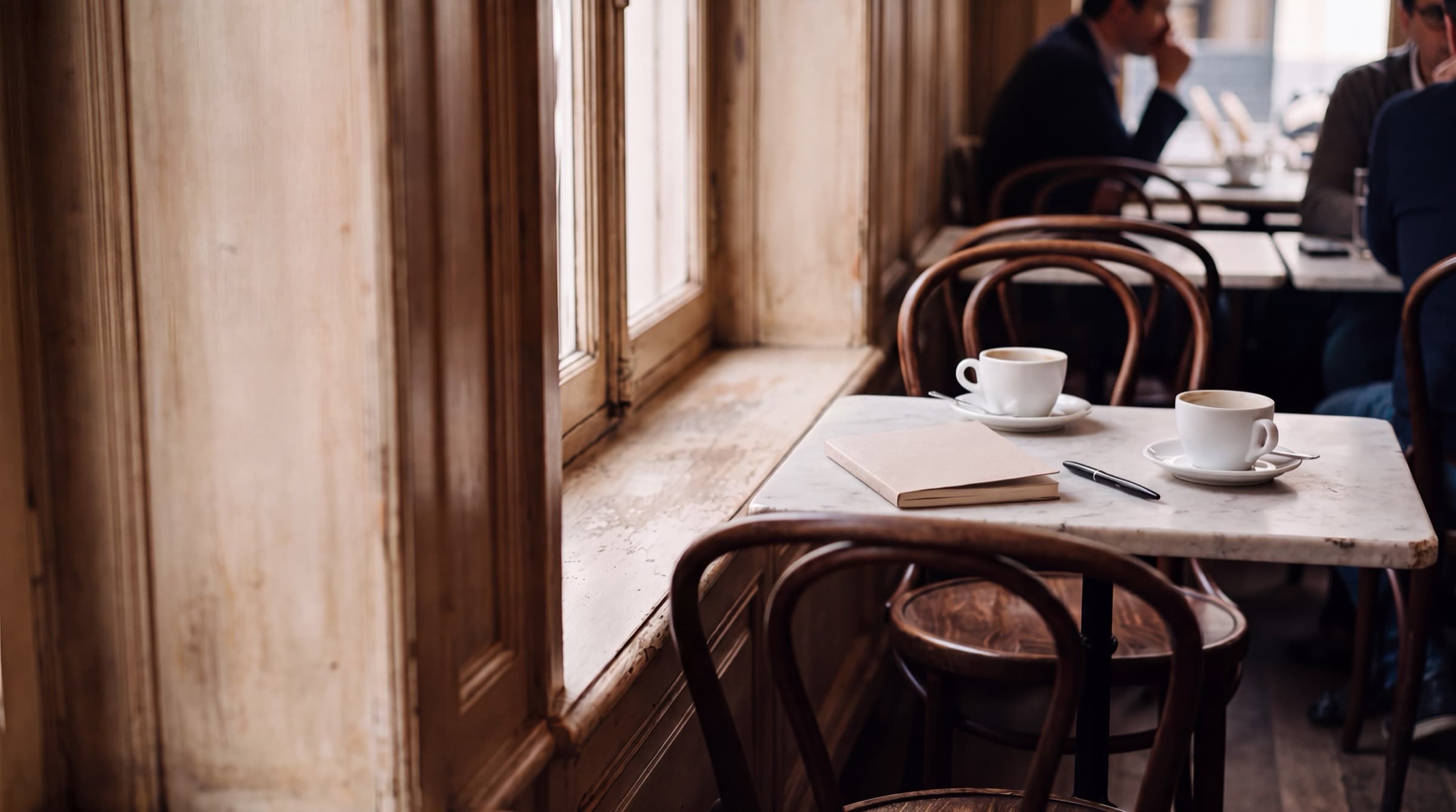 Table de café bruxellois préparée pour un rendez-vous : deux tasses et un carnet